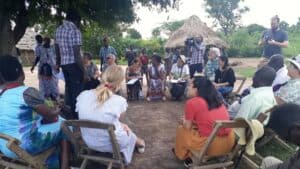 Community members and visitors gathered outdoors for a discussion in a rural village.