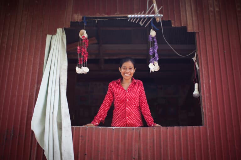 Woman smiling while standing in a window of a home with hanging decorations.