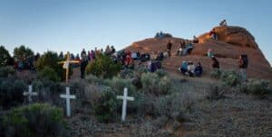 People gathered on a rocky hillside near several wooden crosses during an outdoor prayer service.