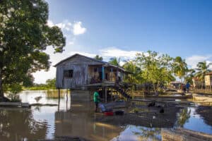 Flooded village with wooden houses and people wading through water.