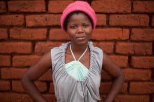 Young girl standing confidently in front of a brick wall.