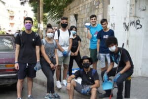 Group of young volunteers cleaning city street with masks and tools.