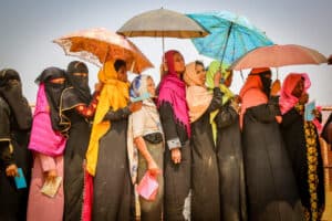 Women and children standing in line with umbrellas during a relief event.