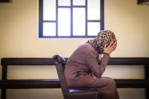 person wearing headscarf sits sideways with hand on bowed head.