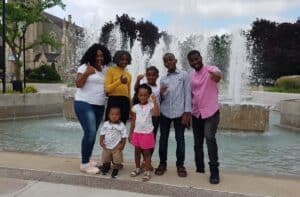 Family group smiling and posing near a fountain in a city park.