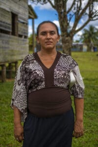 woman wearing brown shirt standing outside with tree and house behind her