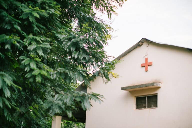 Church building with a red cross and lush green trees nearby.