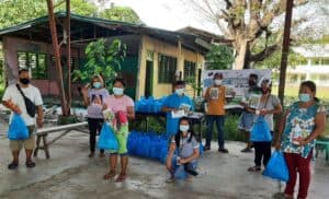 People standing outside social distancing, wearing masks, and carrying blue humanitarian aid bags.