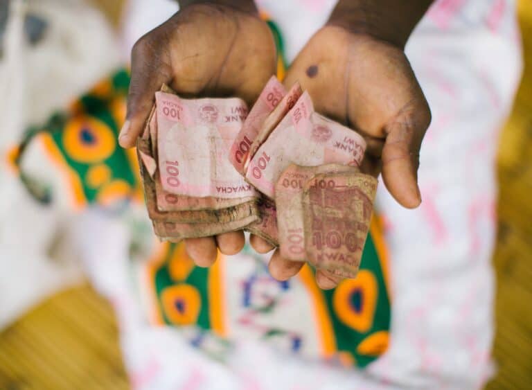 Open hands holding paper money representing community members participating in a village savings and loan group meeting.