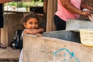 Young girl smiling near water source in a community setting.