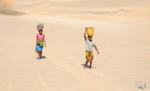 Two children walking on sandy terrain with water containers, Madagascar.