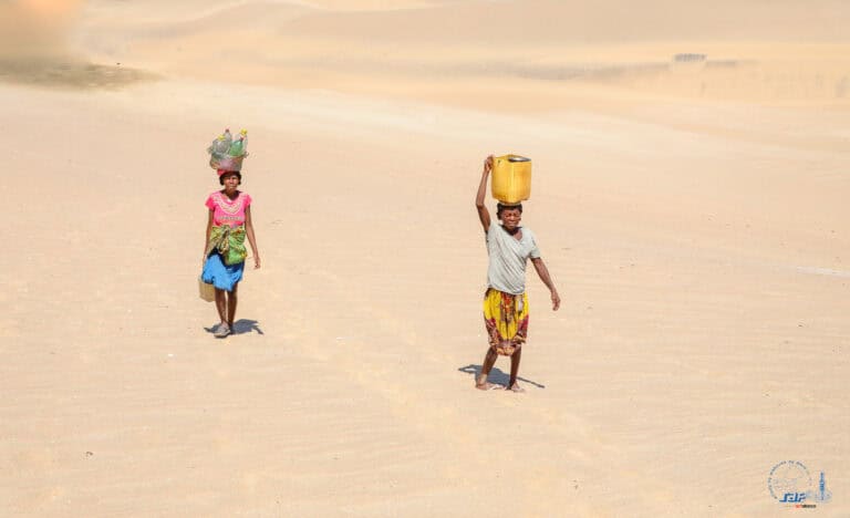 Two children walking on sandy terrain with water containers, Madagascar.