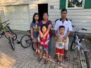 Five people standing in front of a house with several bicycles beside them on a paved driveway.