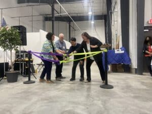 Group of people untying colourful ribbons during a building dedication inside a warehouse space.