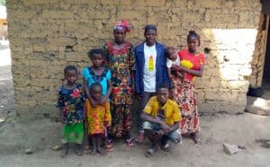 Seven people stand together outside an earthen home in Sierra Leone.