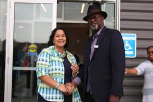 Two people shake hands outside the entrance of a newly completed office building during a dedication event.