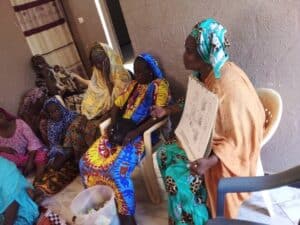 Group of adults seated indoors while a facilitator holds a visual chart and leads a health education discussion.