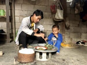 Laotian father and son enjoying a meal together in a modest home.