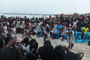 A group of young people perform a coordinated dance outdoors while community members watch.
