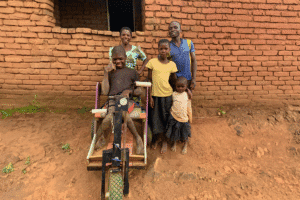 Family with a child in a wheelchair outside a brick house in rural area.