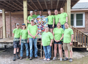 Group of volunteers in green shirts with quilt on construction site.