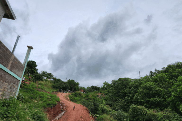 Dirt path winding through lush green hills under cloudy sky.