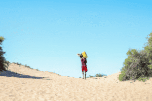 Child with backpack walking in sandy desert under clear blue sky.