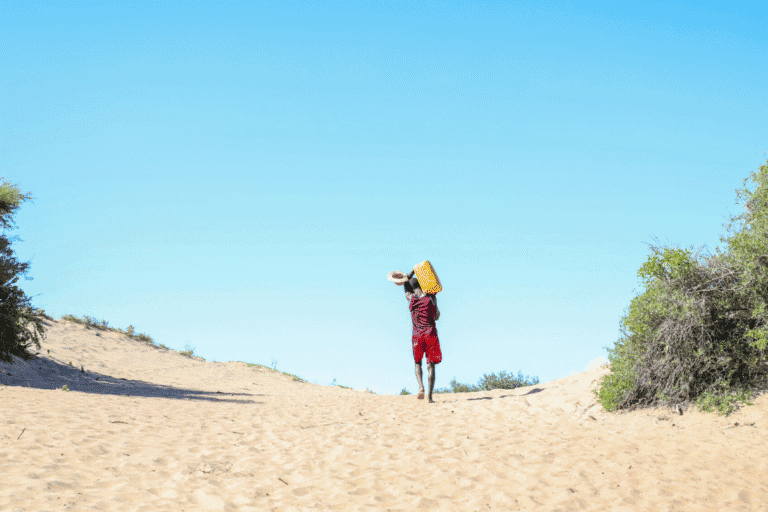 Child with backpack walking in sandy desert under clear blue sky.