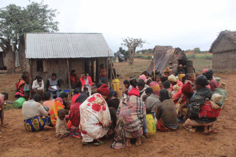 Community gathering of villagers sitting outdoors in a rural setting.