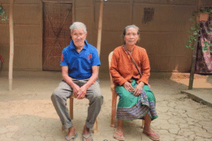 Elderly couple sitting outdoors in a rural village setting.