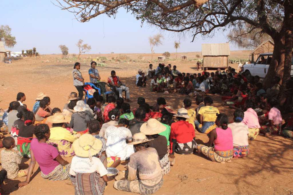 Large community gathering under a tree in Madagascar for aid distribution.
