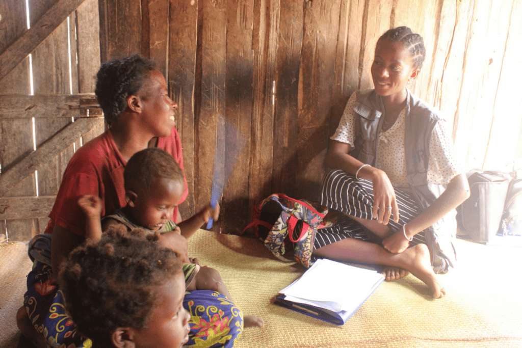 Madagascar community gathering with children and woman inside a wooden hut.