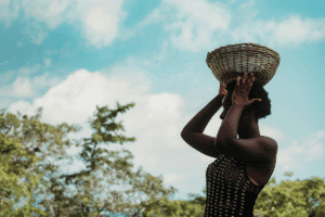 Woman carrying a basket on her head in a rural setting.