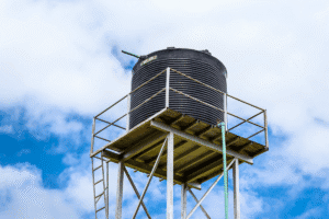 Water tower structure with a black tank against a blue sky.
