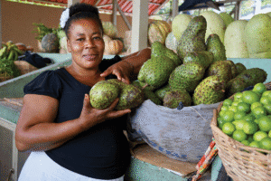 Woman selling fresh soursop and other fruits at local market.