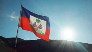 Haitian flag waving in the sunlight over a mountainous landscape.
