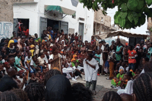 Large community gathering with a speaker addressing a crowd outdoors.