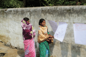 Women hanging posters on a wall for community awareness in rural area.