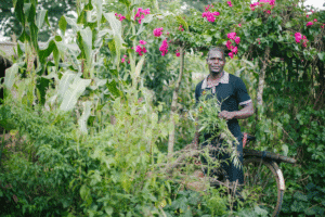 Man standing in lush garden with vegetables and flowers, promoting sustainable farming.