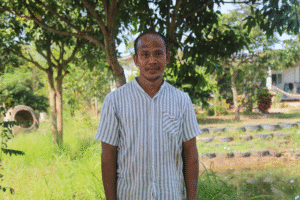Man standing outdoors in a lush green park with trees and grass.