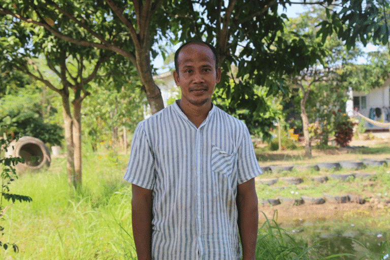 Man standing outdoors in a lush green park with trees and grass.