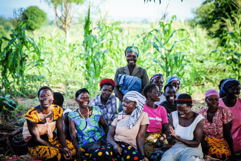 Group of smiling women and men in a lush green farm setting.
