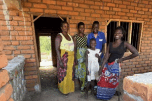 Group of people standing outside a brick house in a rural setting.