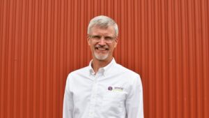 Mike White wearing a white World Renew shirt, standing in front of an orange corrugated wall.