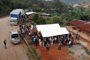 People gathering at a community aid event with tents and trucks in a rural setting.