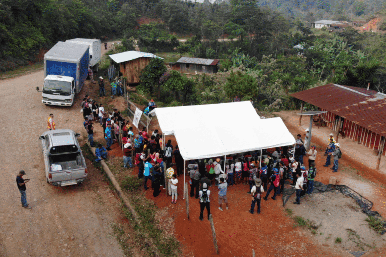 People gathering at a community aid event with tents and trucks in a rural setting.