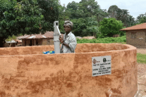 Woman operating a water pump at a community water well in a rural area.