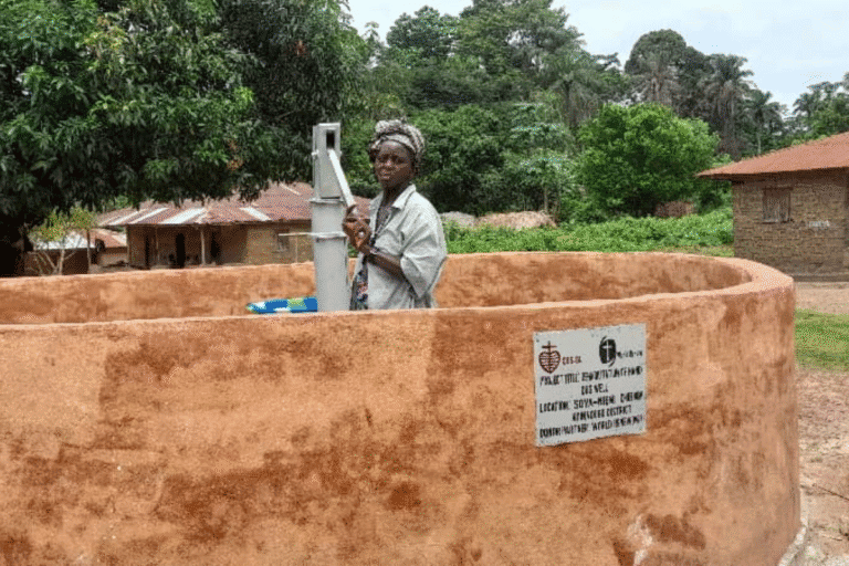 Woman operating a water pump at a community water well in a rural area.