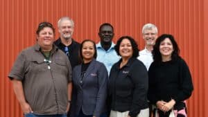 Six World Renew team members standing together in front of an orange wall.