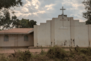 Church building with cross under cloudy sky in rural setting.
